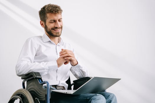 Confident man in a wheelchair working on a laptop indoors with a smile.